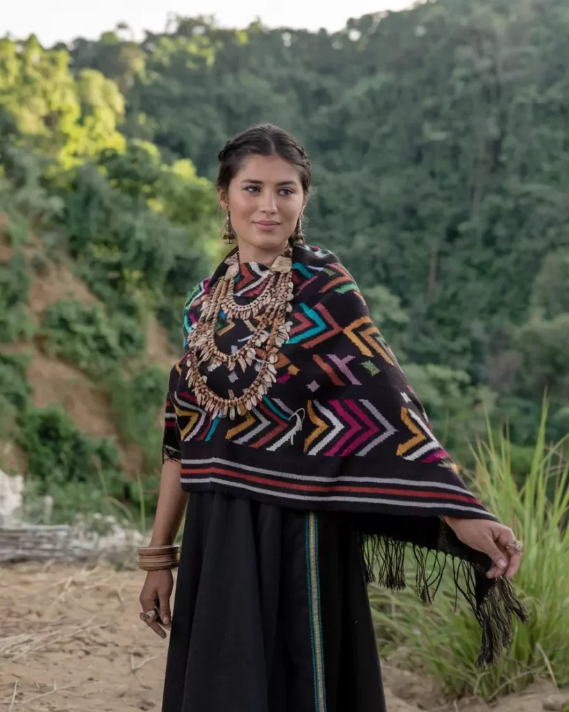 Prompts to Create Beautiful Indian Girls in Diverse Indian Attires AI-generated image of a beautiful Indian girl wearing traditional Nagaland attire featuring a vibrant black shawl with multicolored tribal patterns and layered bead necklaces, standing outdoors, showcasing the rich tribal heritage of Northeast India by AI Artz.