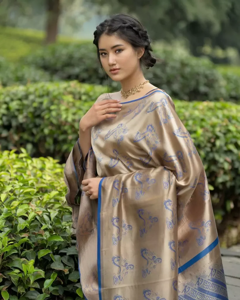 Prompts to Create Beautiful Indian Girls in Diverse Indian Attires AI-generated image of a beautiful Indian woman dressed in a traditional Mekhela Chador from Assam, featuring elegant cream and blue handwoven patterns, styled with gold jewelry and set against lush greenery, showcasing Assam's rich textile legacy and weaving artistry by AI Artz.