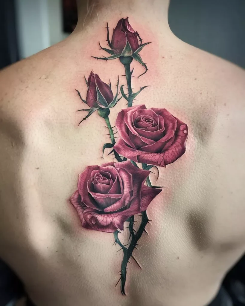 Realistic rose vine tattoo on a person’s back featuring two red roses and two rosebuds with detailed petals and leaves. The dark green vine runs vertically along the spine with sharp thorns, creating a lifelike three-dimensional effect. The design blends floral realism with body art, emphasizing nature-inspired tattoo artistry and precision shading by AI Artz